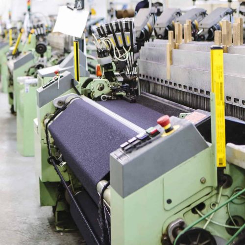 Male factory worker monitoring weaving machine quality in woollen mill